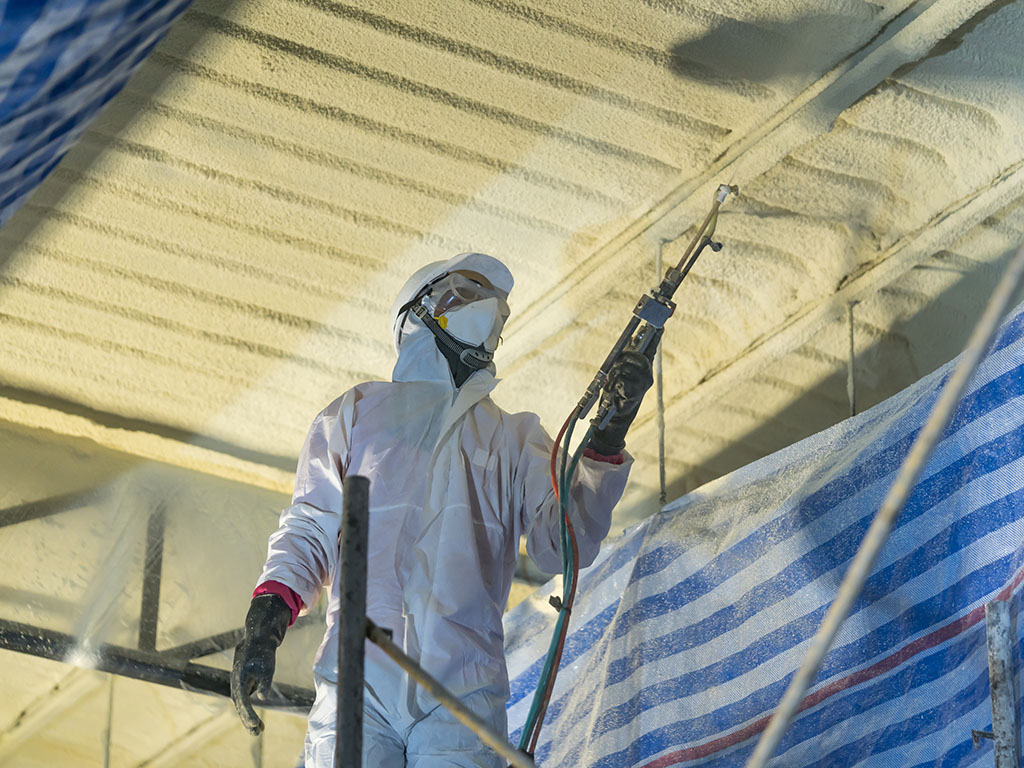 Werknemer in beschermende kleding spuit purschuim op het plafond