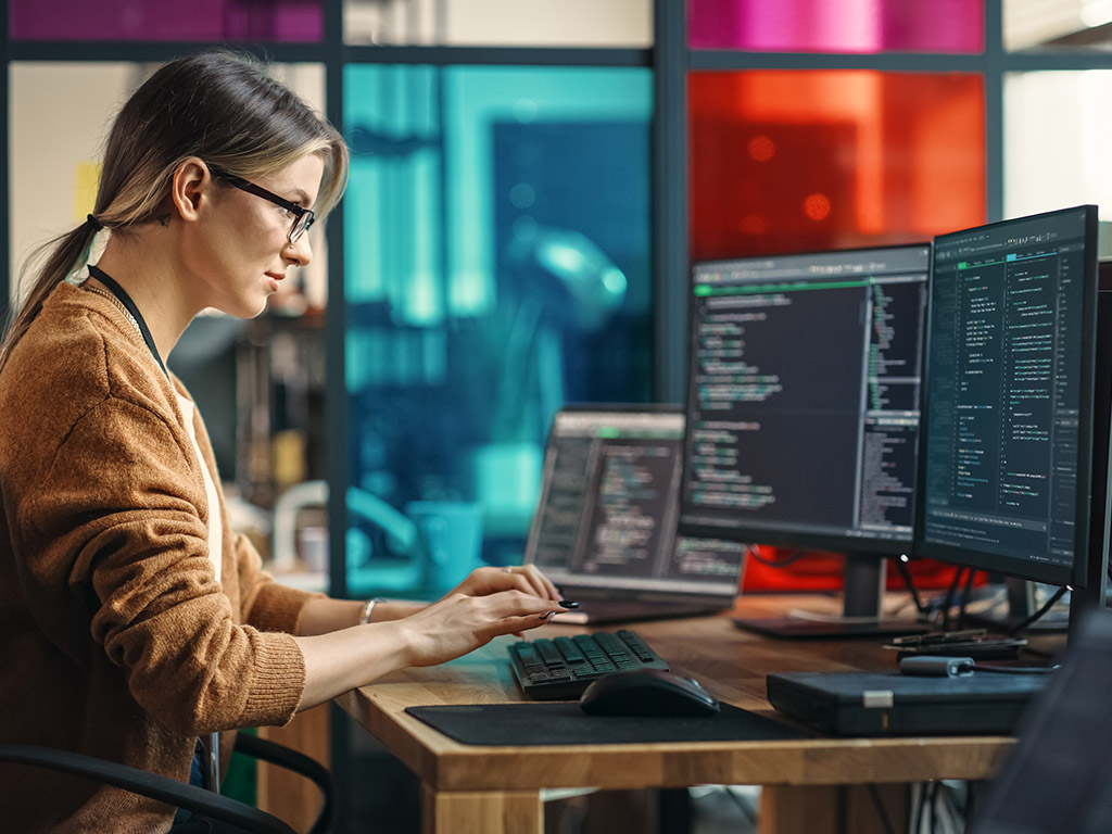 Jonge vrouw aan programmeren op desktopcomputer met twee monitoren