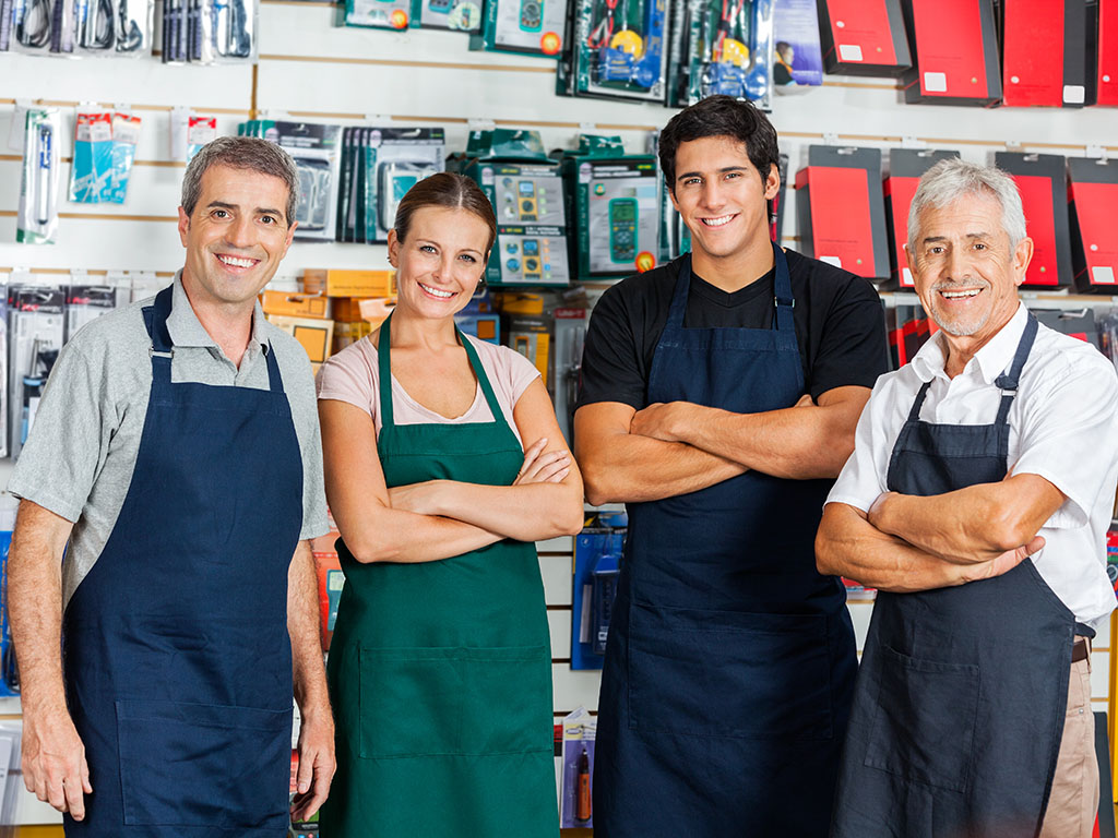 Drie mannen en een vrouw staan voor een wand in een winkel voor kantoorartikelen.