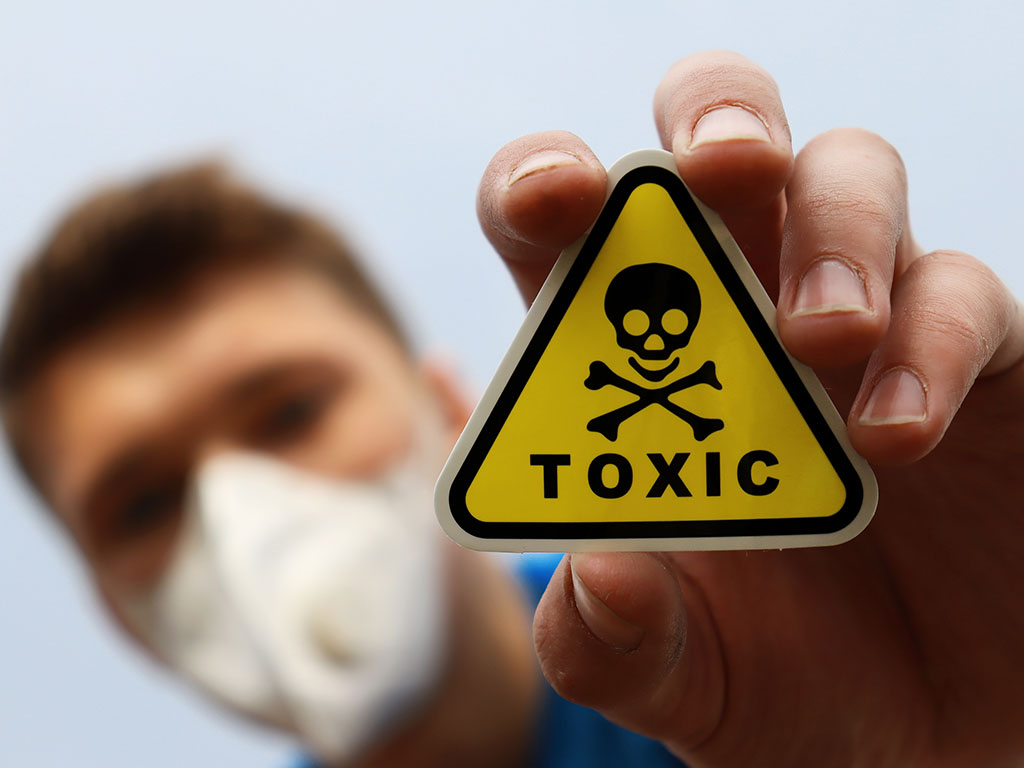 Jonge man die giftig teken in handen houdt. Een geel bordje met skelet en het woord TOXIC.