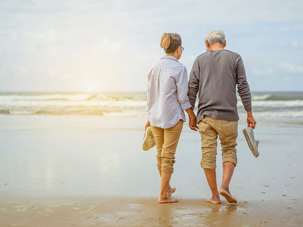 Vrouw en man van middelbare leeftijd lopen op het strand, vanaf de achterkant gezien.