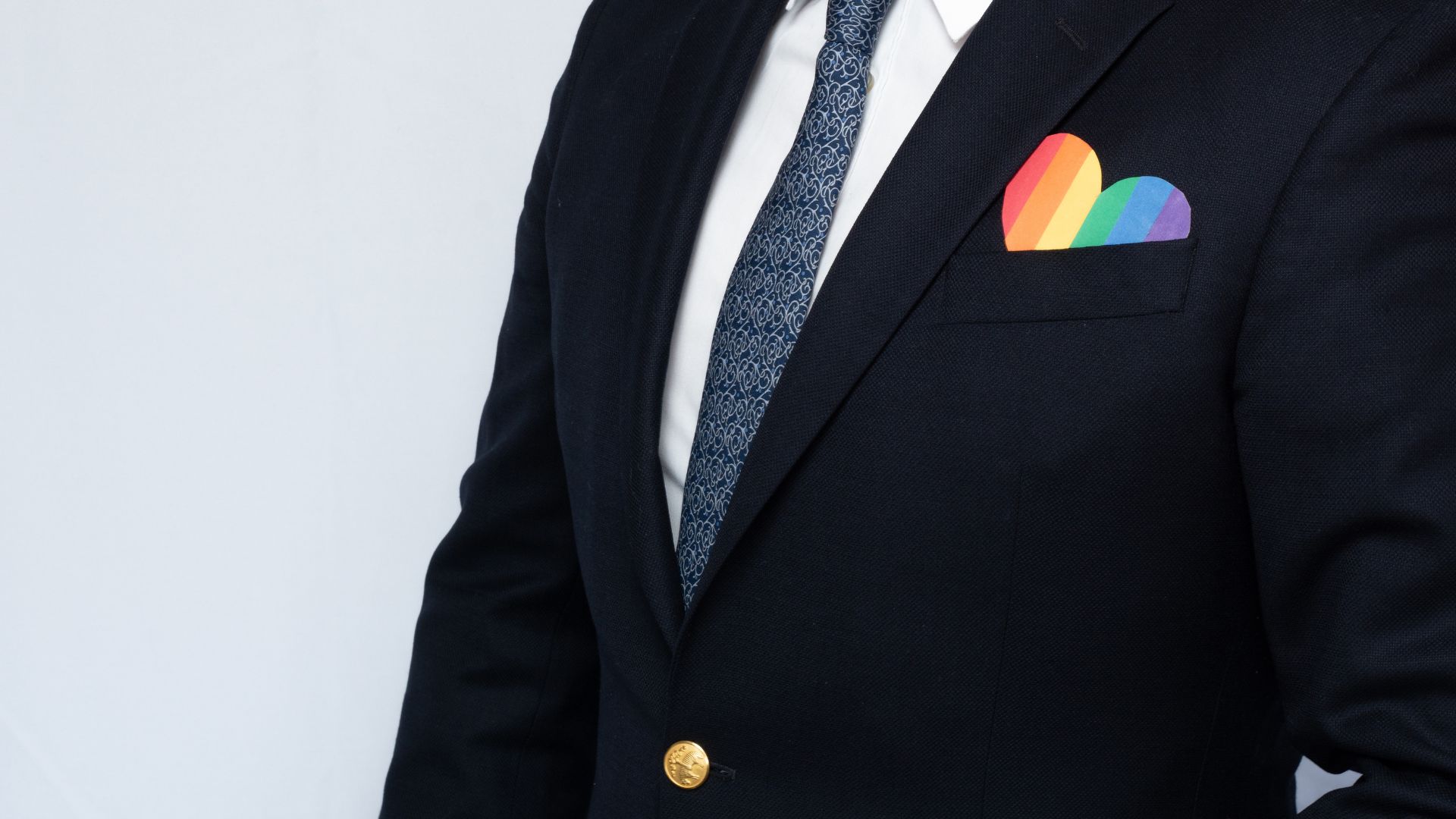 Persoon in pak met hartje in kleuren regenboogvlag in borstzak.