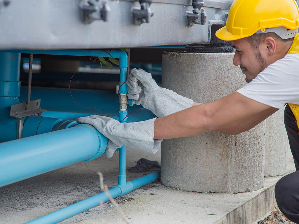 De arbeider met de gele veiligheidshelm repareert de waterleiding onder het gebouw.