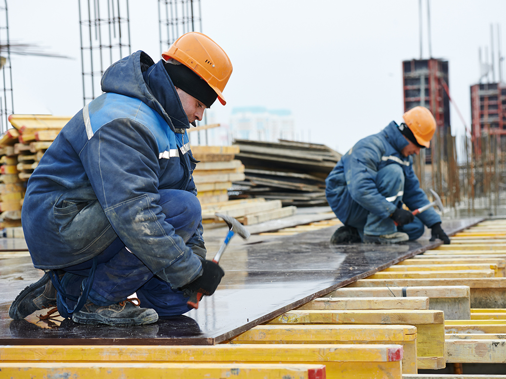 Twee bouwvakkers, warm aangekleed met veiligheidshelm op, aan het werk op een gebouw in aanbouw