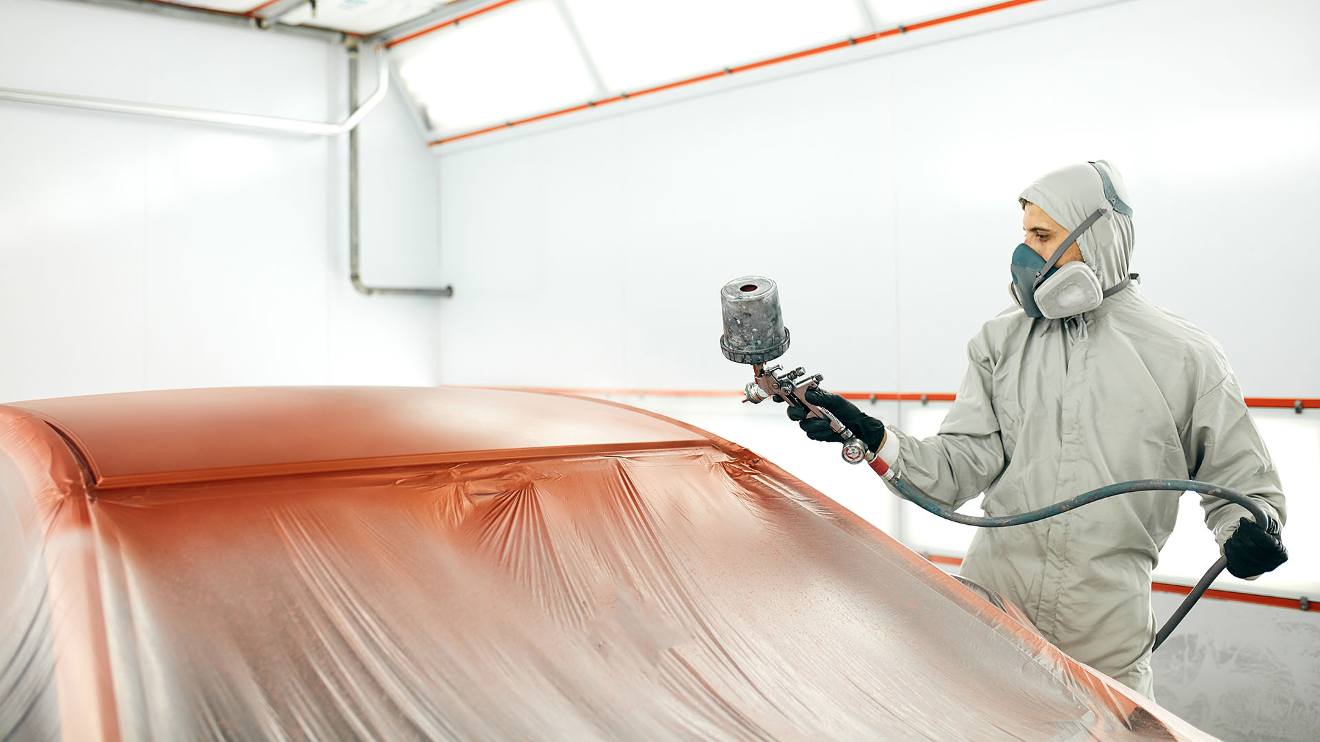 Man with protective clothes and mask painting car roof using compressor.