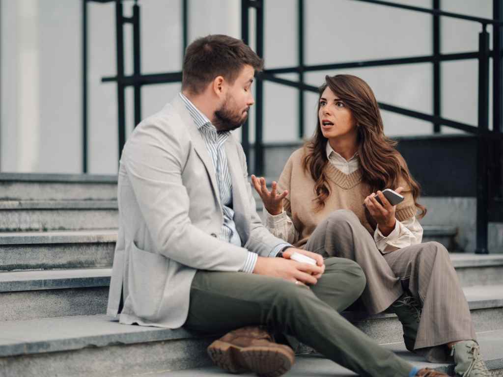 Een vrouw en een man zitten op een trap te praten