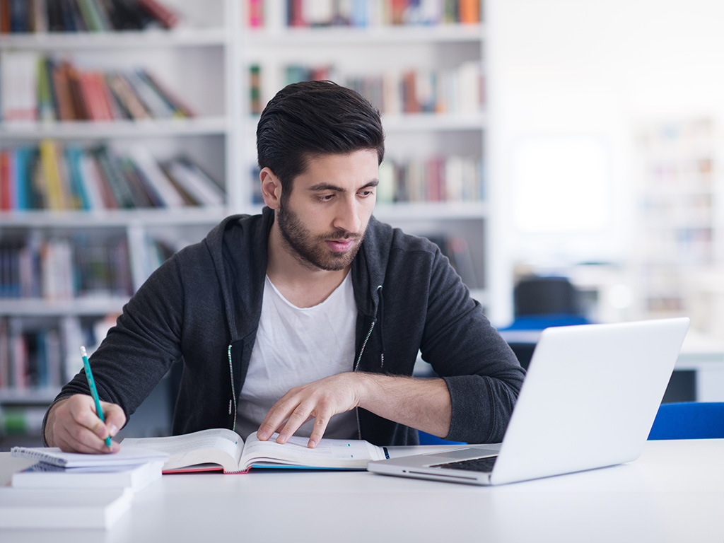 Jongen aan de studie achter laptop en boeken