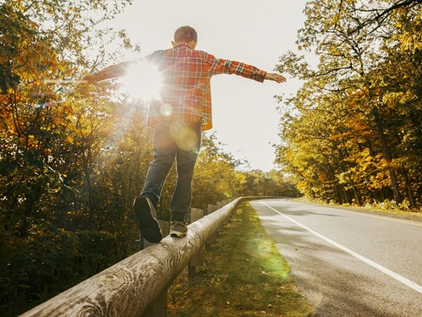 Man balanceert op houten vangrail naast een weg